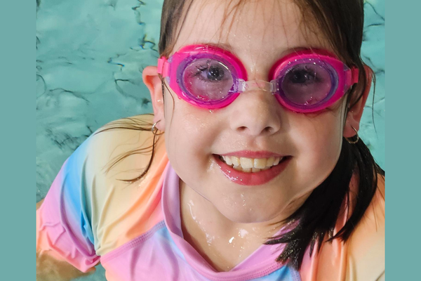 A young girl in goggles smiles up at the camera during her SAIL lessons