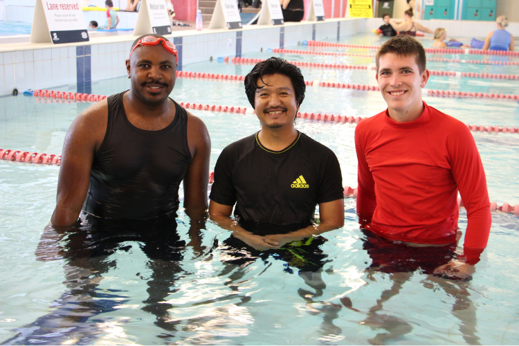 two participants of a men's only swimming lesson standing in a pool with their male pool instructor