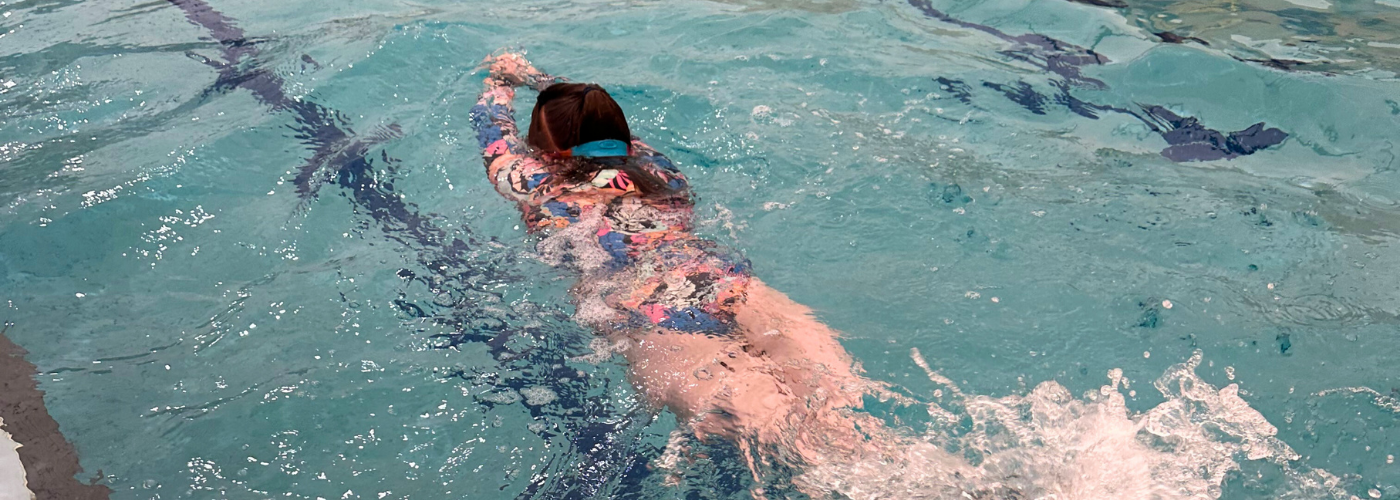 Young girl kicks in the water, facedown in streamline position