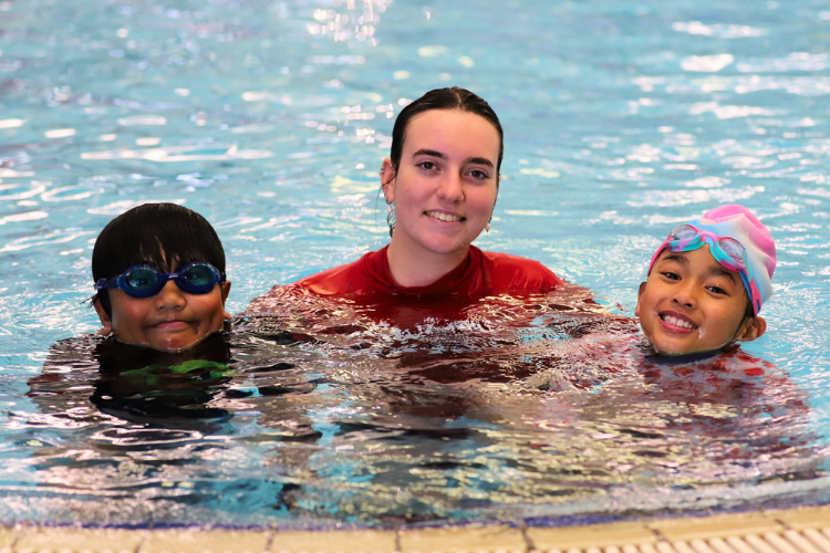 two multicultural children with their swimming instructor in a pool