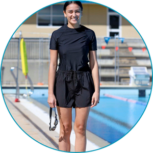 woman wearing short sleeve rashie and swim shorts standing next to a pool