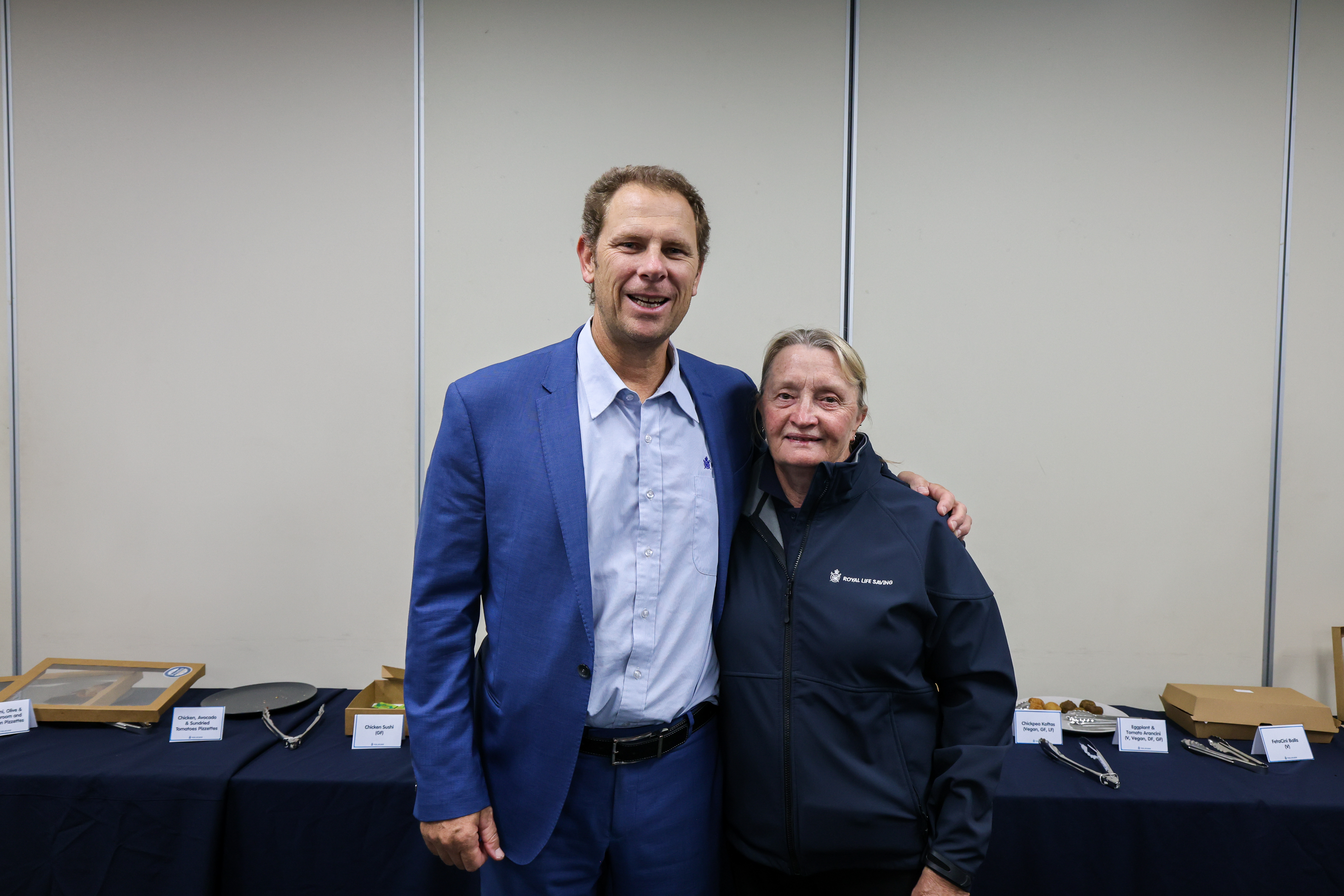 A man in a blue suit stands with his arm around a woman wearing a Royal Life Saving WA jacket at the 2026 AGM.