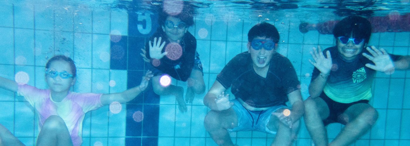 Children underwater smiling at camera