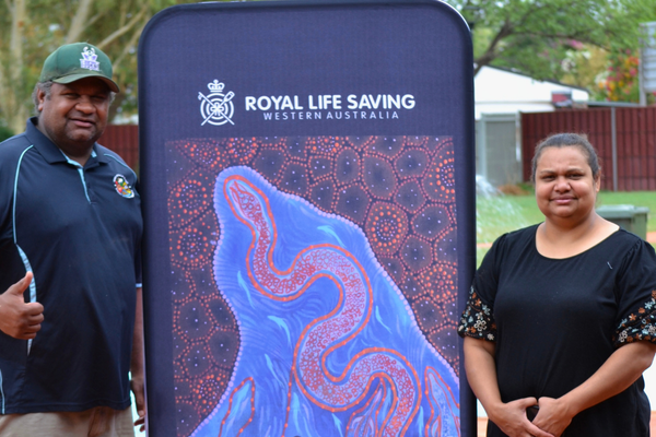 Local artist Deirdre and her husband Halls Creek Sports & Recreational Manager Eldean Mcale stand next to a sign she created for the carnival