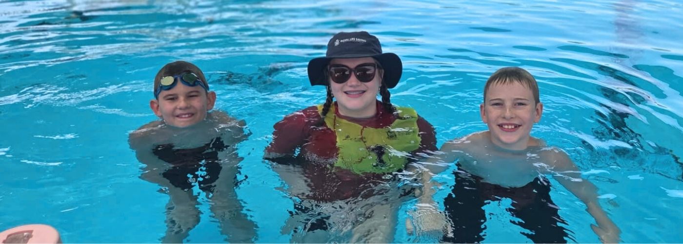 Swim instuctor wearing a hat in the pool with swimming lesson students on either side