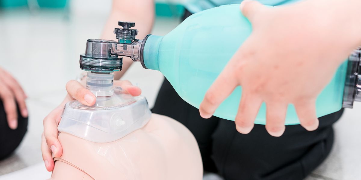 Hand holding the BVM while mask is placed over CPR mannequin face