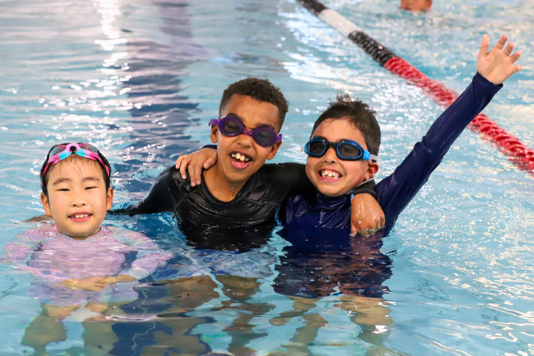 three multicultural children in a swimming pool looking happy