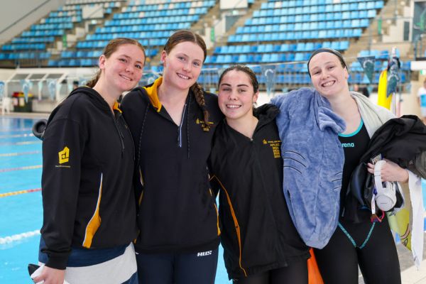 Four female athletes smile together beside the pool at the 2026 Australian Pool Lifesaving Championships.