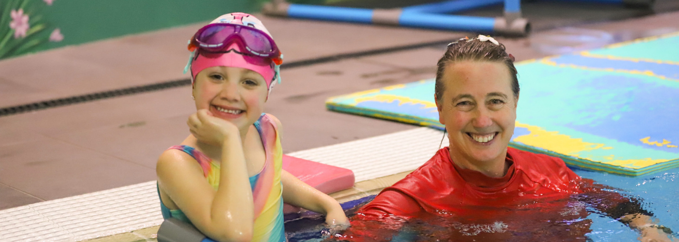 A young SAIL participant smiles up at the camera with her instructor in the pool