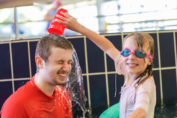 young girl splashing her swim instructor