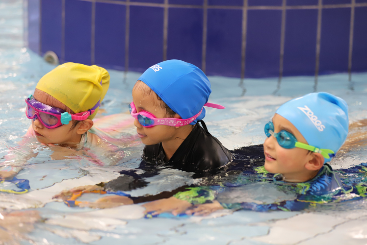 three young children wearing swim caps and goggles at a swimming lesson