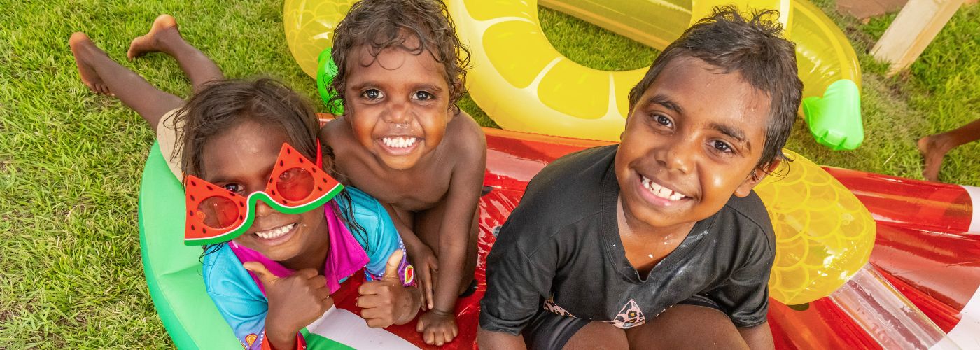 Three children laying on inflatable pool toys smiling up at the camera