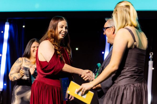 Annika Brown speaks at a lectern, with a screen behind her announcing her as WA Trainee of the Year.