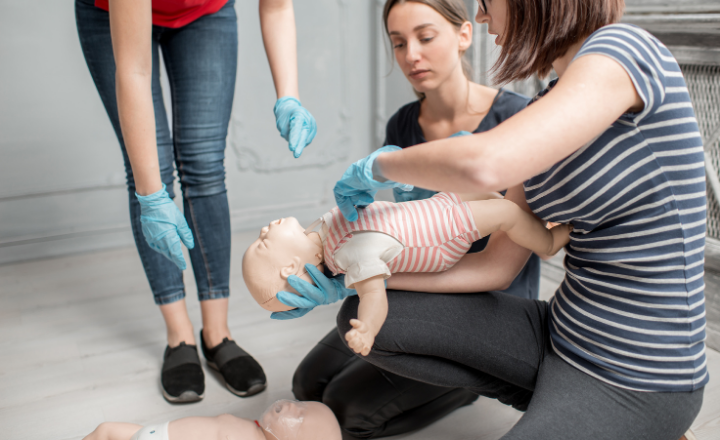 Three women in their 20s with an infant cpr maniking learning about chest compressions
