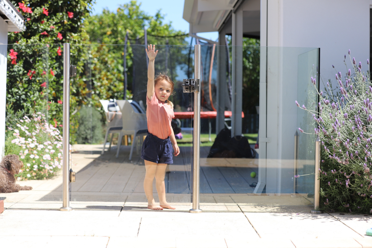 A young girl reaches up to open a glass pool barrier