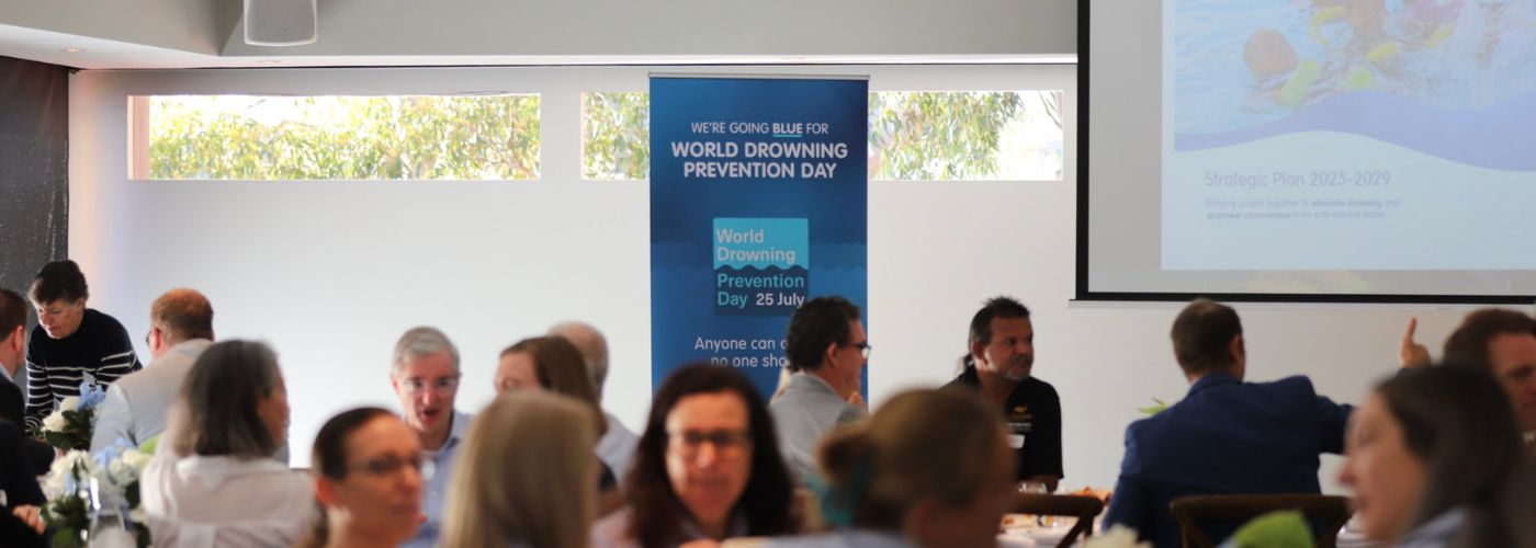 Photo of Matilda Bay Restaurant with World Drowning Prevention Day banner behind seated crowd