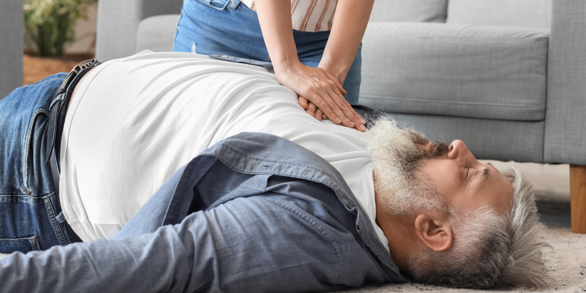 person applying chest compressions to an unconscious male lying on the floor