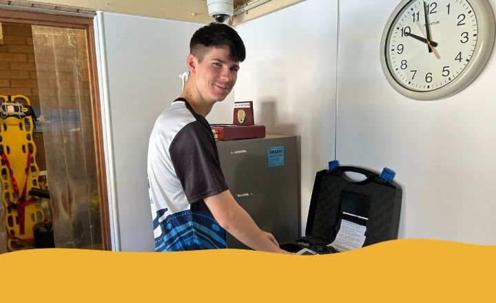 Teenage boy smiling while using pool water testing equipment in a lifeguard office.