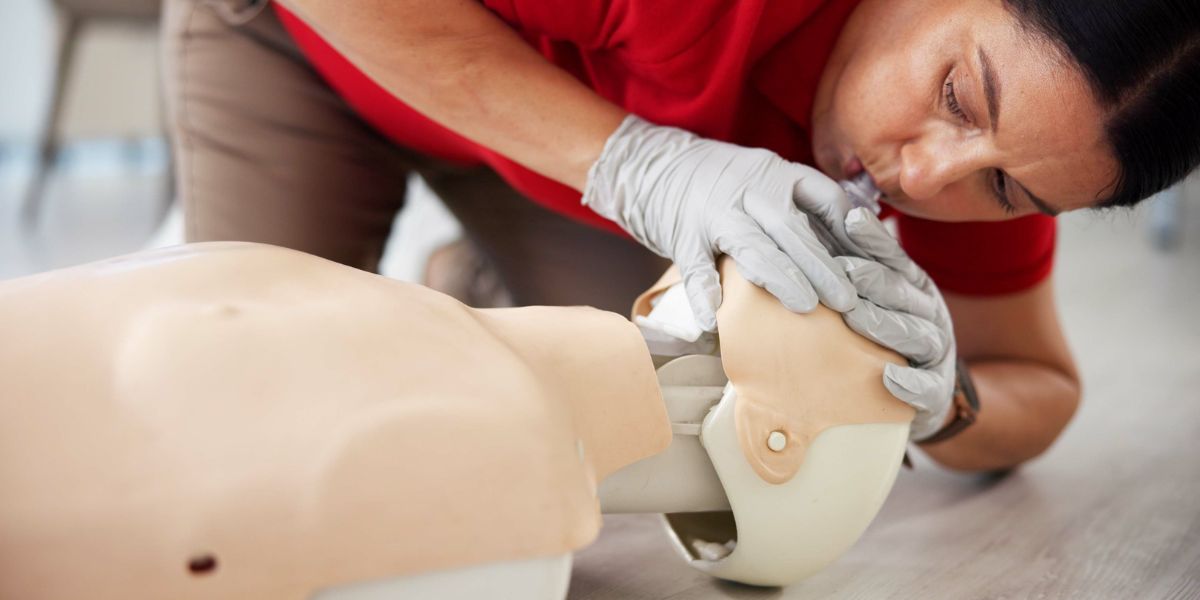 Woman using gloves and face mask to perform CPR on a dummy