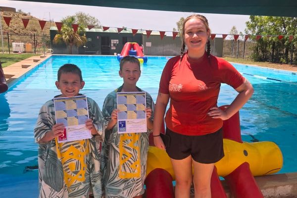 Teacher standing with two students holding certificates out of the water