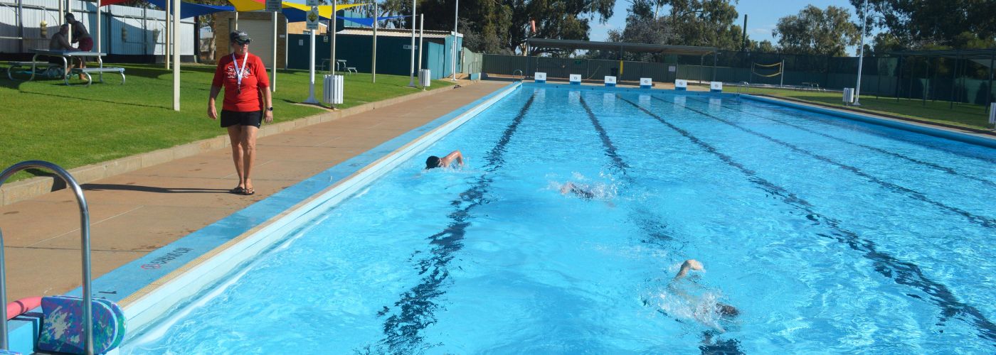 Swim instructor standing on pool edge as children swim freestyle
