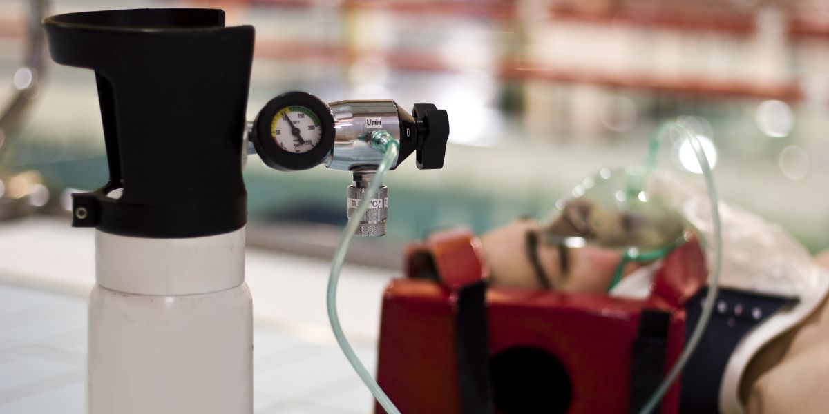 Person in neck brace and face mask with oxygen tank in front of